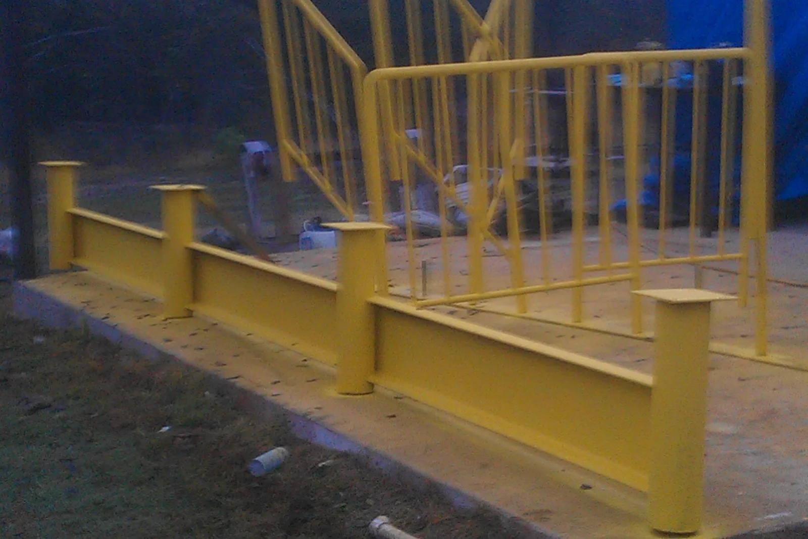 Yellow painted steel guardrail with capped posts and tubular steel stair handrail on concrete landing
