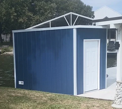 Blue vertical-panel storage shed with white trim and white entry door on a concrete pad