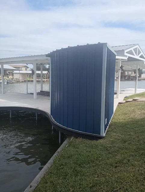 Blue corrugated metal storage enclosure with white trim on a concrete waterfront dock beside a covered boat slip