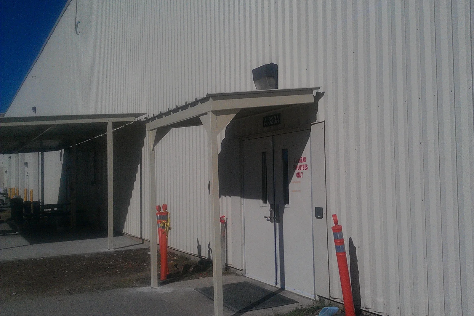 Painted steel entry canopy with metal roof over double doors on corrugated metal building