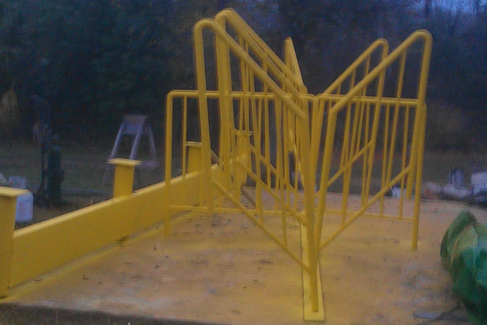 Yellow painted steel pipe railing with vertical balusters installed on a concrete slab with angled guard section