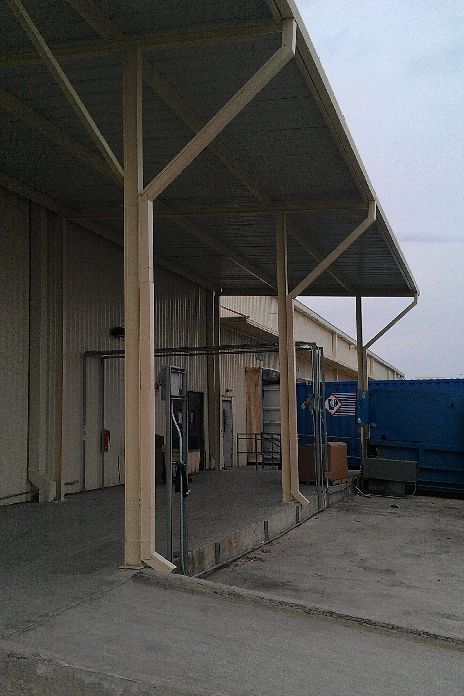 Cream painted steel canopy with corrugated metal roof, diagonal knee braces, and columns over a concrete loading dock