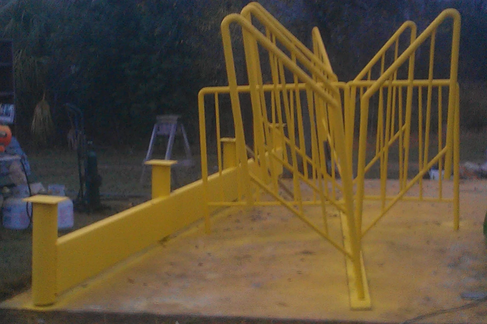 Yellow painted steel ramp with tubular handrails, vertical balusters, and square post caps on a concrete platform