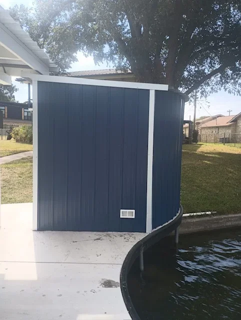 Blue metal panel storage enclosure with white trim beside a curved pool edge on concrete deck