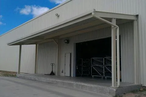 White corrugated metal building with cantilevered steel canopy over concrete loading dock and roll-up door bay