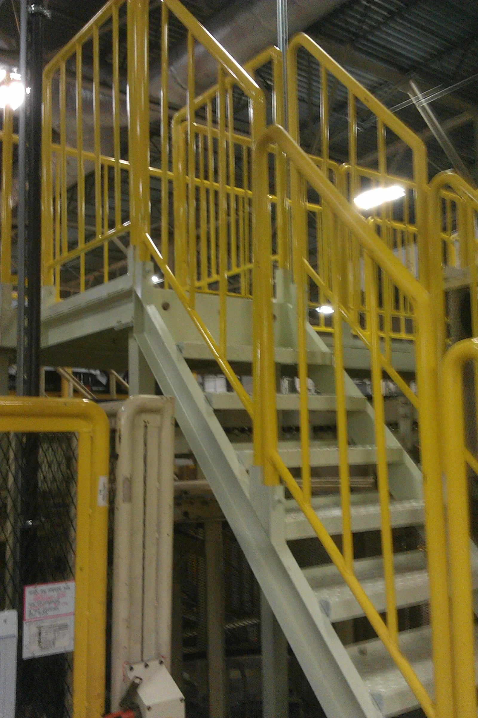 Gray painted steel industrial staircase with yellow tubular safety railings leading to an elevated platform