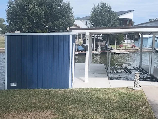 Blue metal-sided storage shed with white trim beside a covered boat lift on a concrete dock