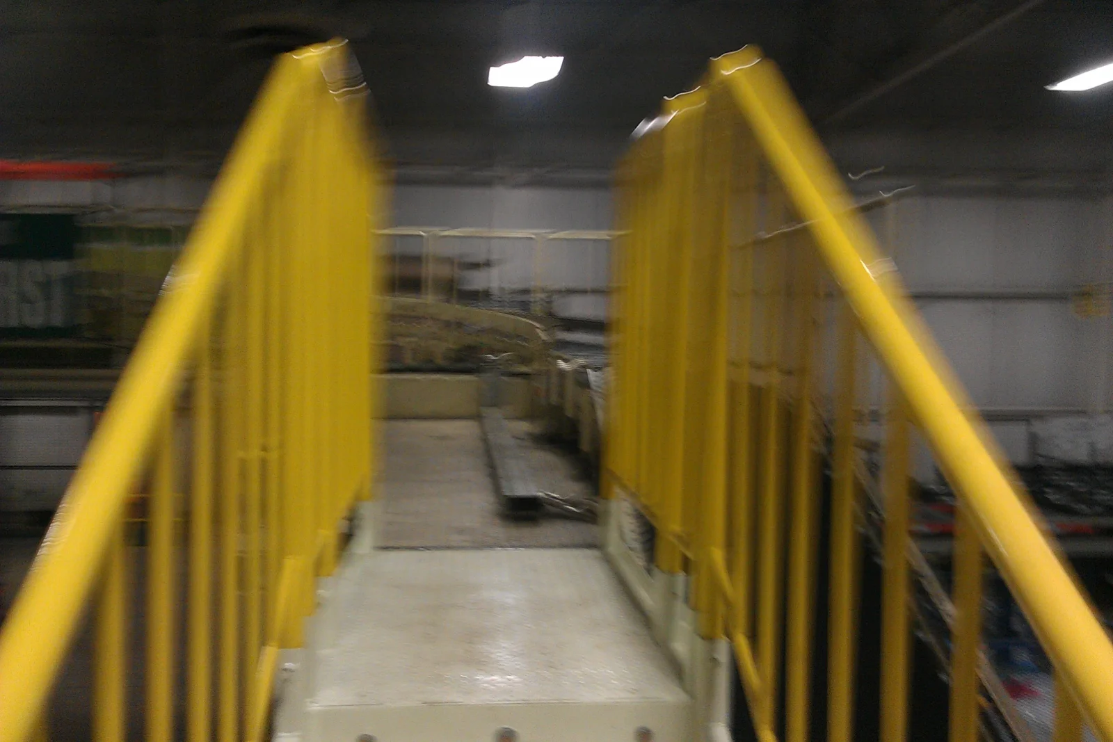 Yellow painted steel safety railings with vertical balusters along a raised concrete walkway in an industrial interior