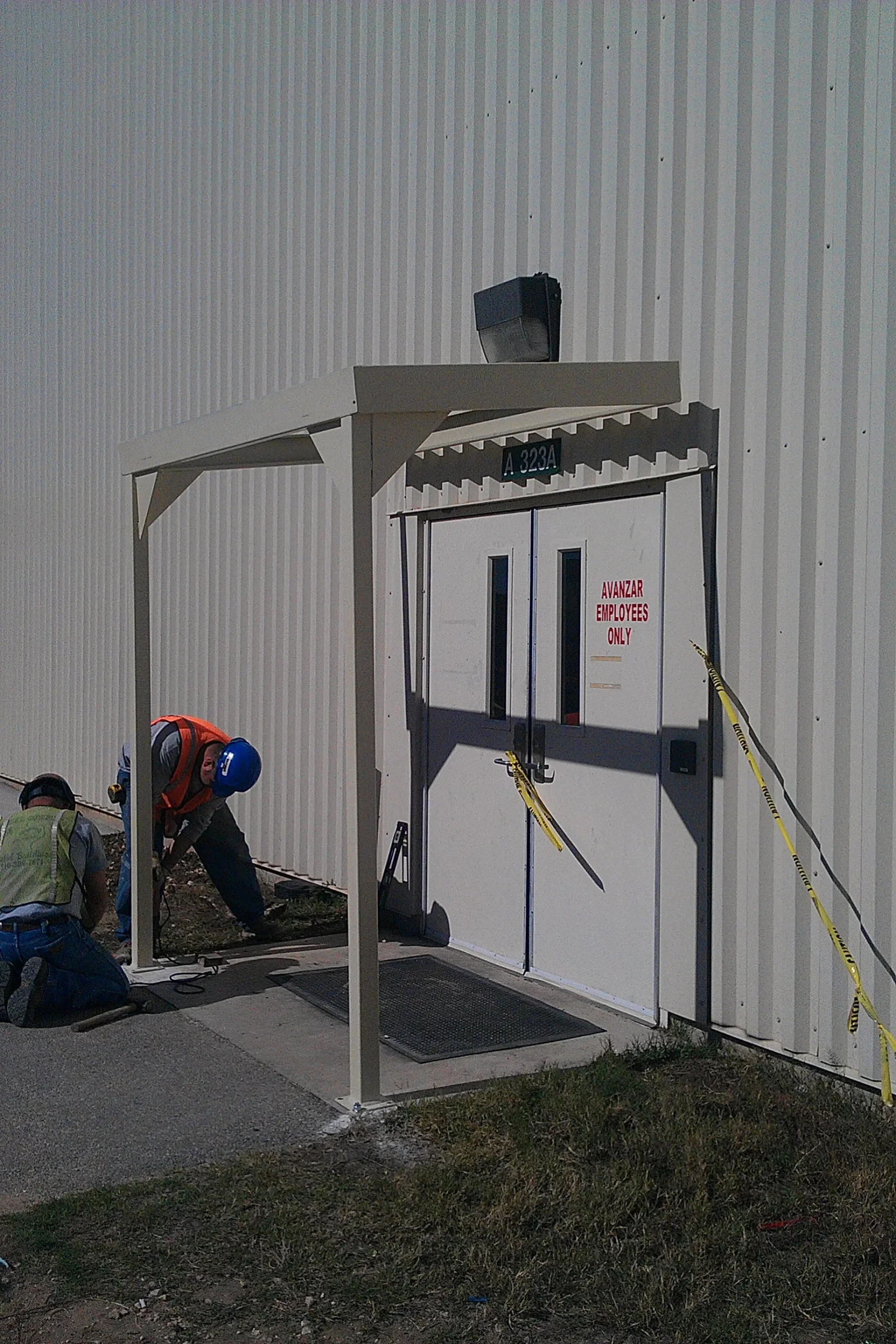 Steel entry canopy with tubular posts and gusset brackets being installed over a double door on corrugated metal wall