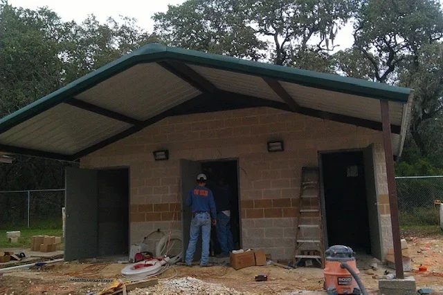 Concrete block storage building under construction with sloped metal roof, dark green trim, and exposed steel rafters